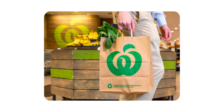 Image shows a person holding a grocery bag with a Woolworths logo on it. 